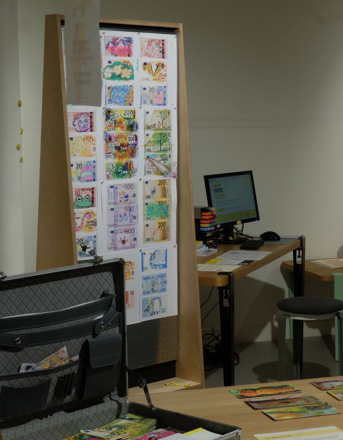 Le mur de billets dessinés et une mallette ouverte, dans l'agence de la banque fantôme